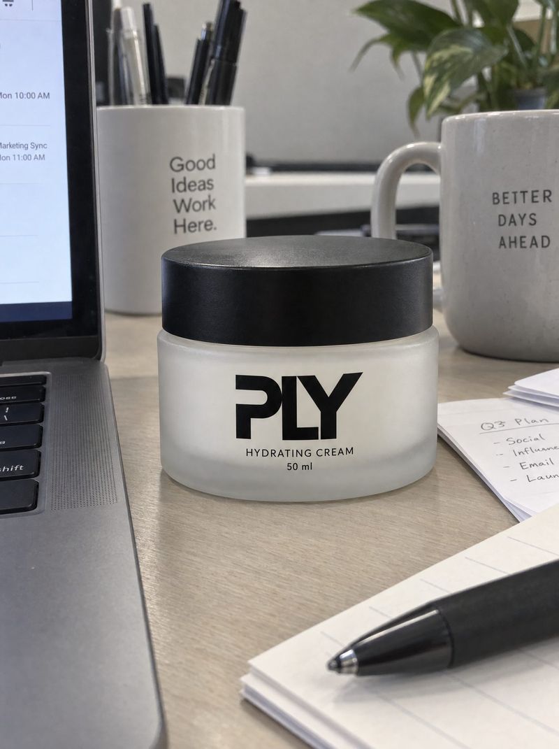 Handyfoto: PLY-Cremetiegel auf einem Schreibtisch neben Laptop und Tassen
